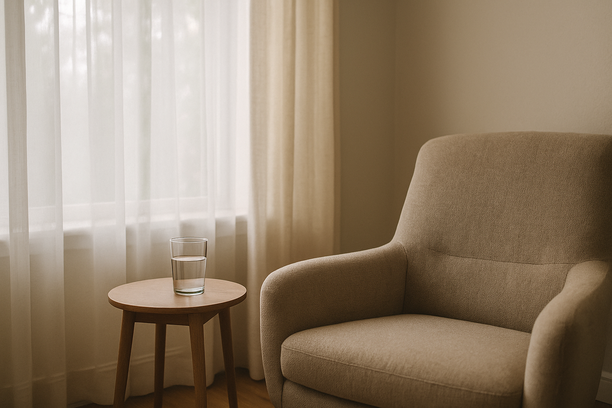 alt_text: A softly lit living room corner with a chair and a glass of water on a side table.